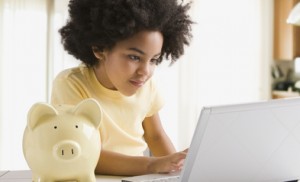 Mixed race girl using laptop next to piggy bank